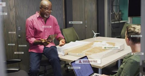 Senior architect presenting sustainable site model with wind turbine and blueprints in meeting