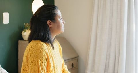 Asian Woman Contemplating by Window in Cozy Living Area