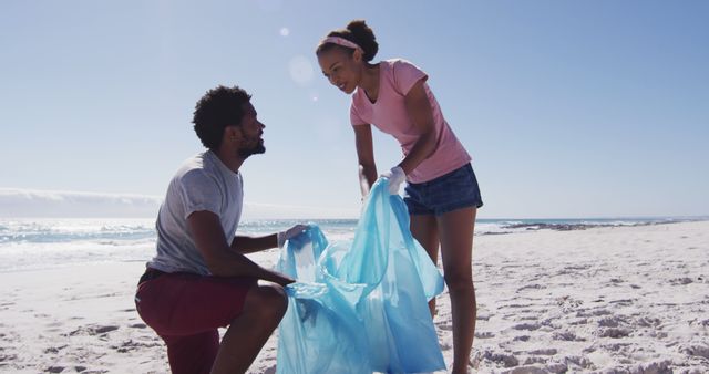 African american couple high fiving, holding rubbish sacks and collecting rubbish from the beach. eco beach conservation.