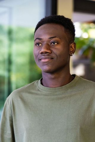 African american man standing by window wearing olive tee looking thoughtful and confident