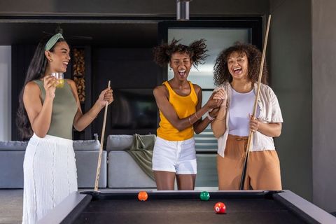 Diverse female friends laughing, playing pool and holding cues in modern game room