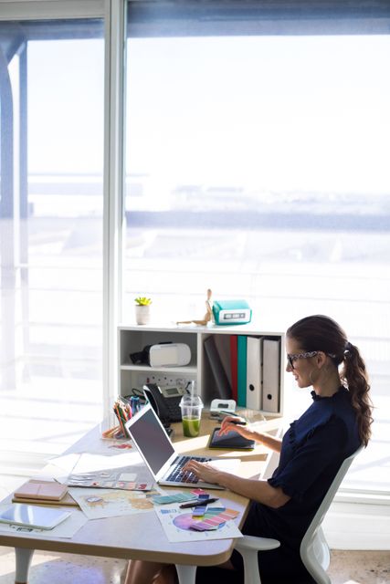 Female executive working over laptop and graphic tablet at her desk in office