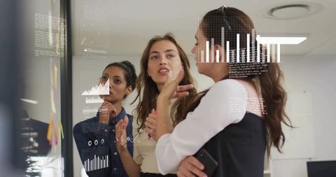 Women Collaborating around Glass Wall with Data Visualizations and Sticky Notes for Analytics