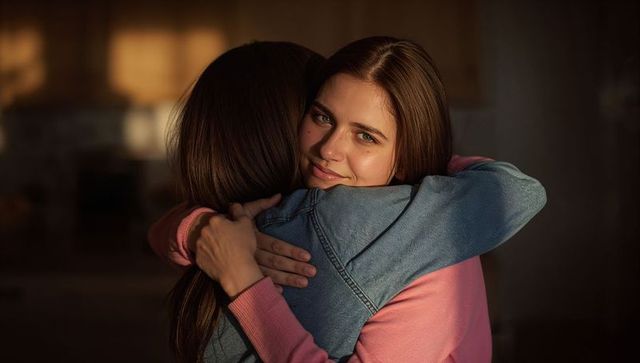 Young women hugging in warm lamp light, intimate home embrace conveying comfort and support