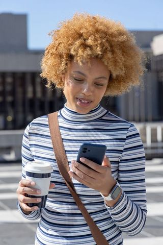 African american woman checking phone while holding coffee on city rooftop terrace