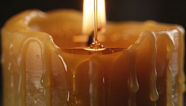 Melting amber candle dripping wax into central pool with flickering flame