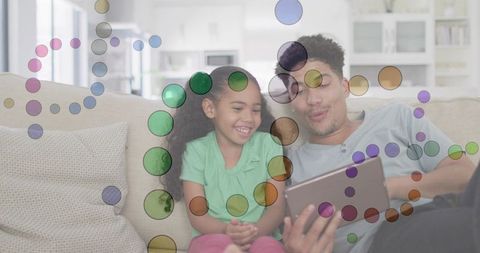 Father and daughter exploring tablet on sofa with colorful digital overlay