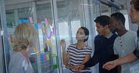 Diverse team collaborating and brainstorming around glass planning wall with Post-it notes