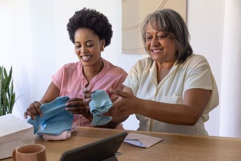 Senior woman and african american woman folding pastel baby clothes while smiling