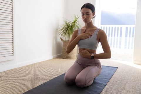 Woman practicing mindful breathing kneeling on yoga mat in bright coastal apartment for wellness