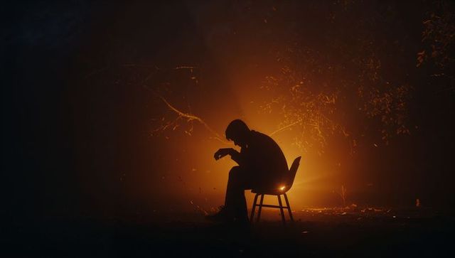 Sitting silhouette of contemplative man on chair with amber backlight in foggy forest