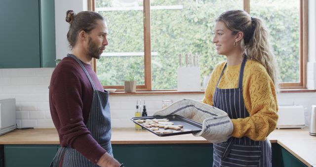 Couple happily baking cookies together in modern kitchen, emphasizing teamwork and domestic life. Perfect for use in content related to cooking, recipes, home lifestyles, and relationship building.