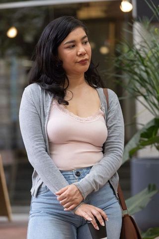 Young woman standing outside storefront holding coffee cup and bag wearing casual denim