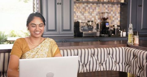 Smiling Indian Woman Using Laptop in Modern Kitchen Home Office