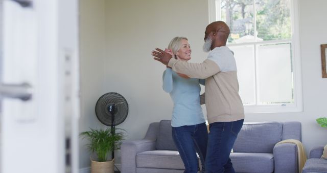 Elderly couple dancing and smiling in living room expressing joy and love. Perfect for themes related to senior lifestyle, happiness, relationship harmony, and celebrating life. Ideal for advertisements, brochures, and websites focusing on elderly care and living, joy in old age, and close family bonds.