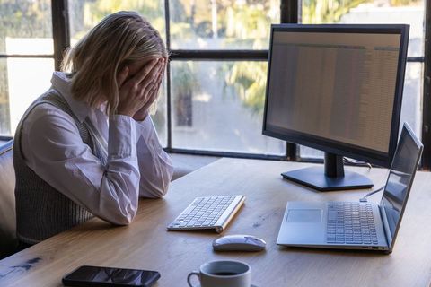Stressed businesswoman at desk covering face with hands in modern office