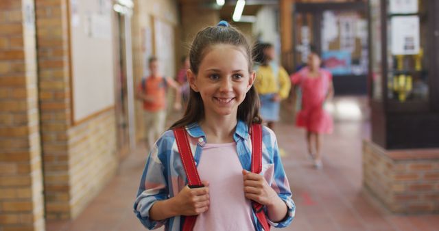 Cheerful young girl is carrying a backpack while walking through a school corridor. Perfect for depicting education, back-to-school themes, elementary school promotional materials, and academic-related content targeting young students and childhood experiences.