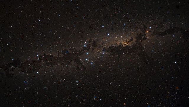 Milky way band stretching across night sky with dark dust lanes and galactic bulge