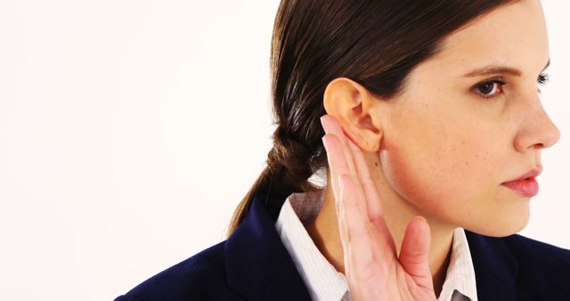 A young Caucasian woman appears to be listening intently, with her hand cupped behind her ear to enhance her hearing. Her focused expression suggests she is trying to discern a distant or quiet sound.