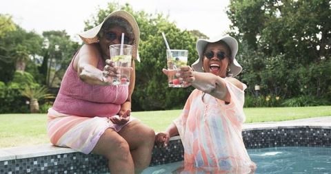 Senior Friends in Pool Toasting with Drinks Under Sunhats
