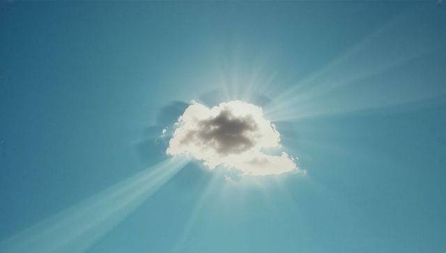 Glowing White Cloud with Radiant Sunrays in Clear Blue Sky
