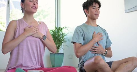 Diverse couple meditating at home wearing smartwatches practicing mindful breathing