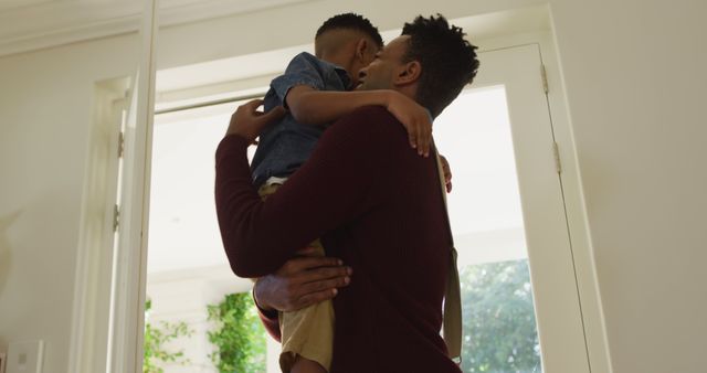 Father holding young son in tight hug in cheerful home doorway. Ideal for family-themed marketing materials, parenting blog illustrations, or advertisements promoting family values and bonding moments.