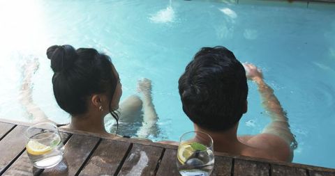 Diverse couple relaxing at pool edge with lemon-mint drinks on wooden deck