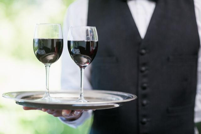 Mid section of male waiter holding tray with wine glasses in restaurant