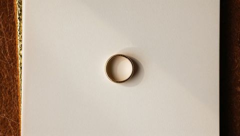 Gold wedding band casting soft shadow on cream card with leather and gold-foil trim