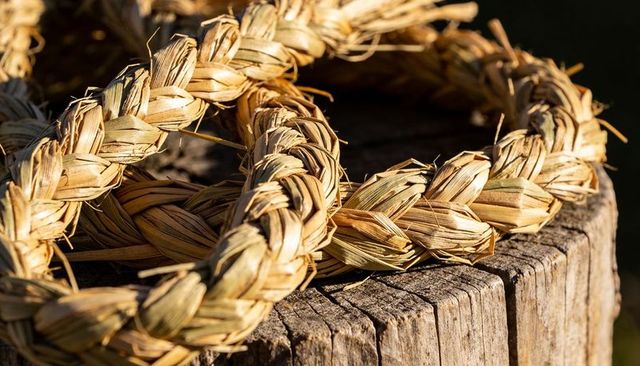 Sunlit braided straw rings resting on weathered wooden stump showing golden textured fibers