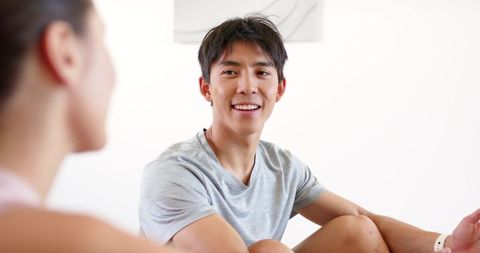 Smiling asian man relaxing and talking with partner in bright modern living room