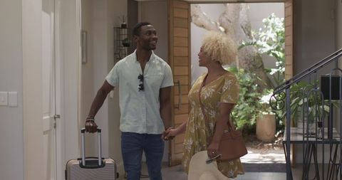 Smiling couple entering home with luggage on sunny day