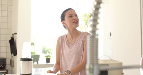 African american woman preparing smoothie in bright kitchen wearing smartwatch and smiling