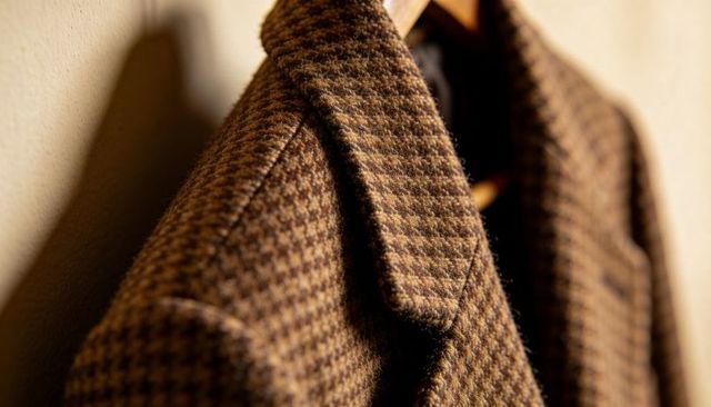 Hanging brown houndstooth wool coat on wooden hanger in warm hallway closeup texture detail