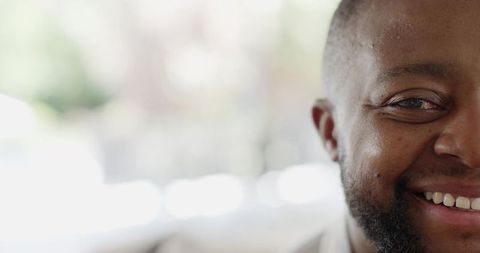 Smiling man showing teeth closeup with trimmed beard and warm bokeh background