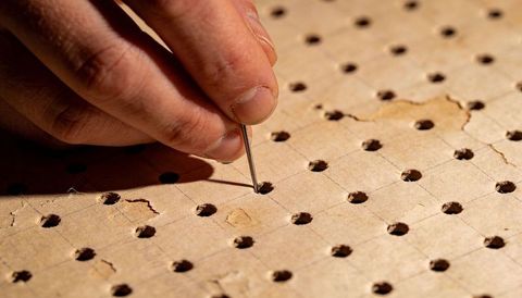 Hand placing metal pin into perforated pegboard showing torn fibers and grid holes