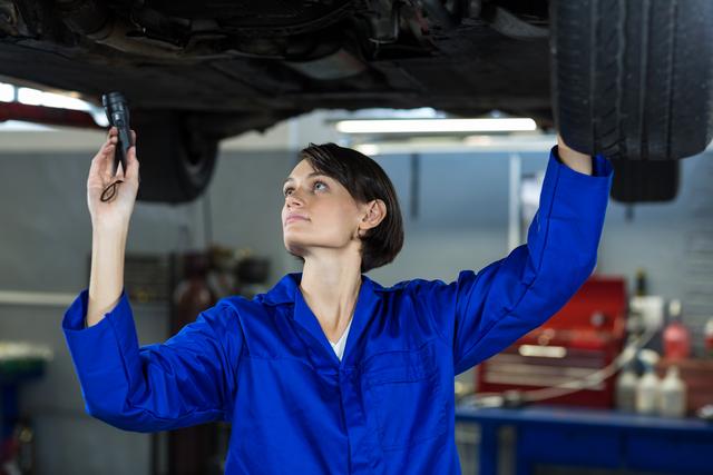 Female mechanic examining a car with flashlight in repair garage