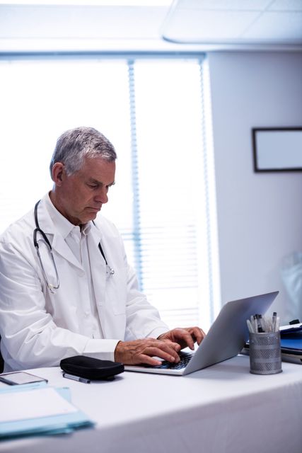 Doctor sitting at table and using laptop in clinic