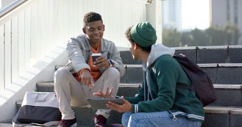 African american college friends studying outdoors on campus steps sharing tablet