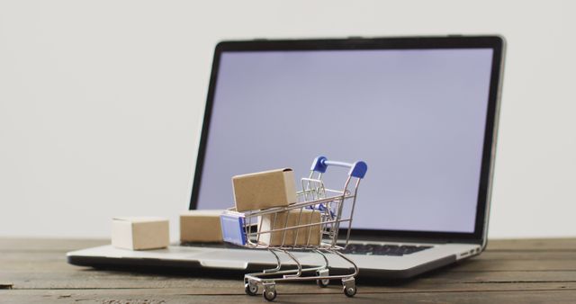 Image depicting an online shopping concept with a laptop and a miniature shopping cart with small packages. Suitable for use in digital marketing materials, e-commerce websites, technology blogs, and retail business presentations.