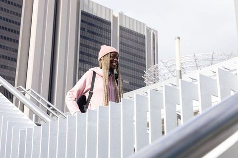 African american teen climbing urban staircase wearing pink hoodie backpack smiling