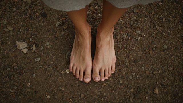 Bare feet standing on dirt trail with gravel and shorts hem, overhead view