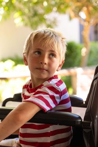 Contemplative young boy in red-and-white striped shirt sitting in stroller outdoors
