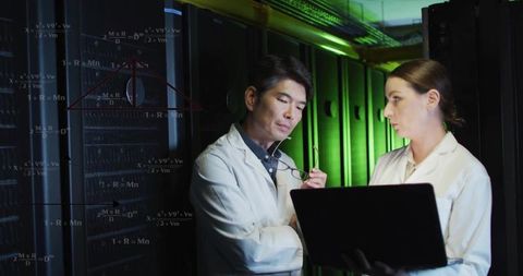 Technicians collaborating in data center room reviewing laptop with projected diagrams