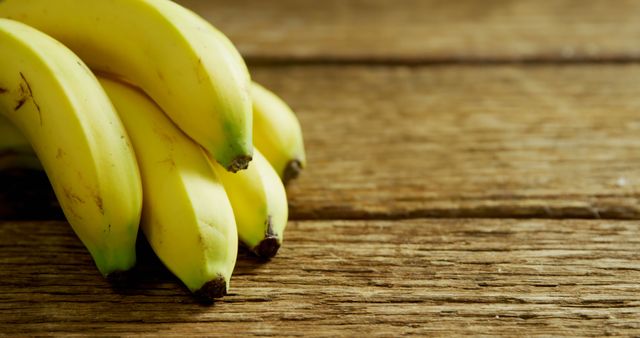 A bunch of ripe bananas rests on a textured wooden surface, with copy space. Bananas are a nutritious fruit rich in potassium and fiber, often included in a healthy diet.