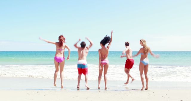 A diverse group of young people is joyfully jumping on a sunny beach, with copy space. Their playful action captures the essence of carefree summer days and friendship.