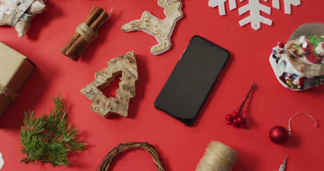 Christmas flat lay featuring smartphone, natural decorations, and pine needle branches on red background. Useful for holiday marketing, festive social media posts, and digital greeting cards.