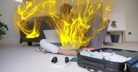 Remote worker typing on laptop with glowing yellow digital particles and open suitcase