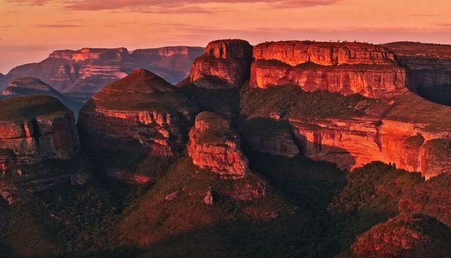 Sun-bathing sandstone mesas and dramatic canyon cliffs over lush green valleys at sunset